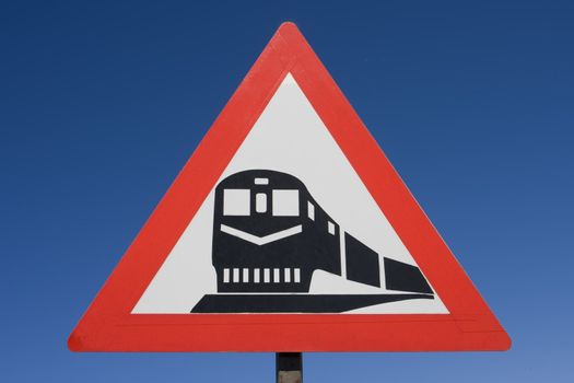 Red black and white rail road caution sign against a brilliant blue background