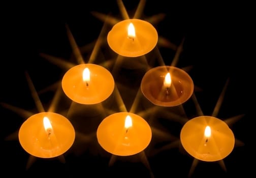 a group of six burning candles on the black background