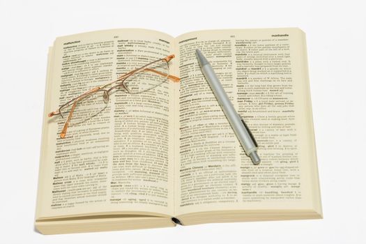 Reading glasses and pen on dictionary, pen pointing at management