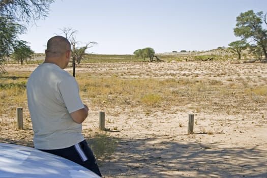 Traveller sitting on the bonnet of his vehicle in the Kalahari