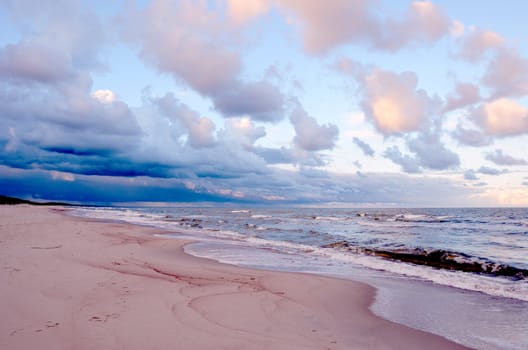 Sea waves climbing on sandy shore. Wonderful cloudy evening sky.