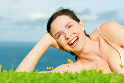 Beautiful young happy woman laying in green grass with yellow flowers