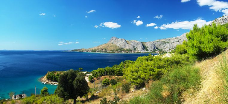 Adriatic Sea coast in Omis in Croatia. Sunny Mediterranean summer landscape. Mountains in the background. Blue sky with clouds. Clean blue sea. Panoramic photos.
