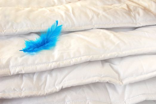 white folded cotton duvet background with blue feather