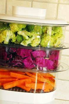 green broccoli, magenta cabbage and orange carrots in steamer