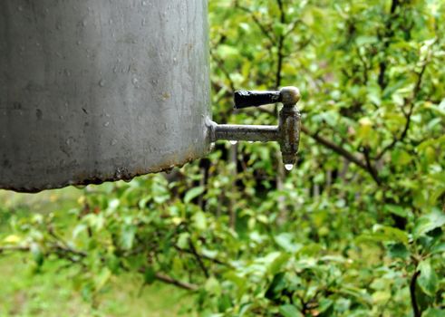 water tap with drops on rustic metallic container outdoors