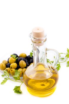 Olives and oil in jug with greens over white