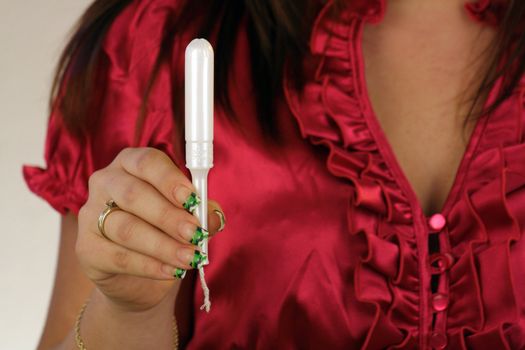 A young woman with camouflage fingernail tips holds a tampon.  Selective focus on the tampon.