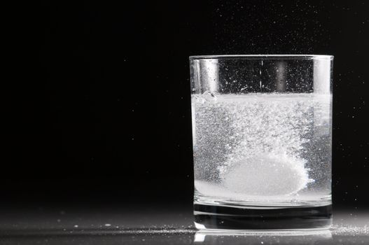 Effervescent pill in a glass of water in backlight