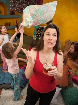 Unhappy Caucasian mom with drink caught with children throwing pillows