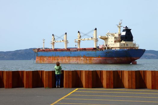 A woman taking photographs of a cargo ship in Astoria Oregon.