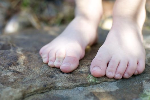 A boy's bare feet stand on top of a smooth slate stone outside on a spring afternoon.