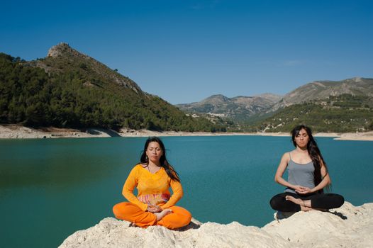MOther and daughter, yoga at beautiful lakeside setting