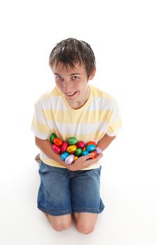 Boy holding an armful of colorful chocolate easter eggs and smiling.  White background, 