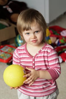 Cute little girl with yellow ball at home with toys on background