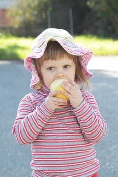 Photo of a cute little girl eating apple outside