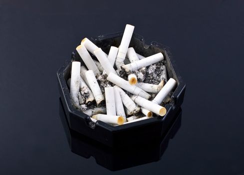 black ashtray with cigaretes on black table