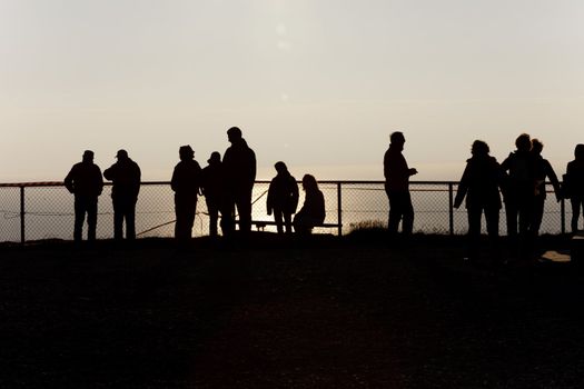 Silhouettes of people at the fence over a cliff