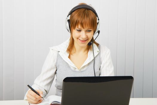Attractive girl in a white blouse with a laptop in headphones with microphone
