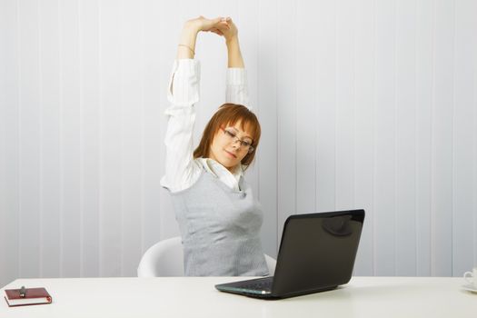 tired girl with a laptop stretches in the workplace