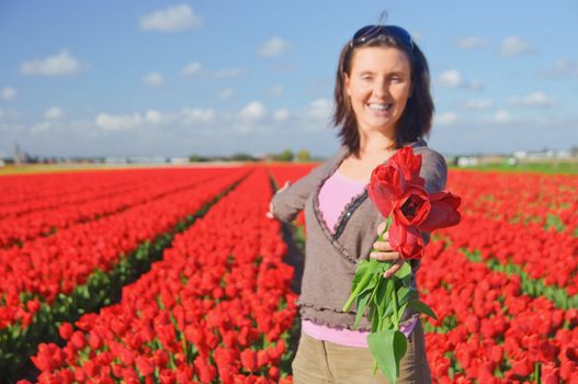 Happy women with red tulip in tulips field. Focus on the bouquet