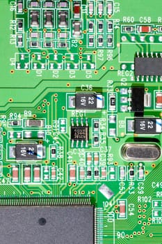 Green circuit board with electronic components such as microchips, condensors, resistors, and transistors.