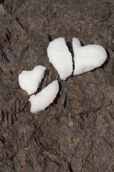 Two broken hearts formed from snow on rock surface symbolizing shattered love.