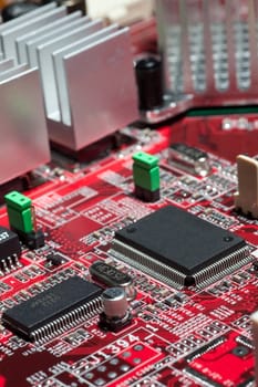 Red circuit board with electronic components such as microchips, condensors, resistors, and transistors.