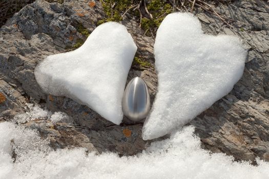 Two Valentine�s Day Hearts formed from snow and steel egg on rock surface.
