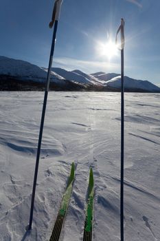 Cross country skiing. Skies and poles on frozen mountain lake. Perfect winter snow conditions with blue sky and bright sun shine.