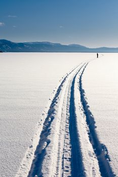 A person skiing in a snowmobile track on vast surface of frozen Lake Laberge, Yukon T., Canada