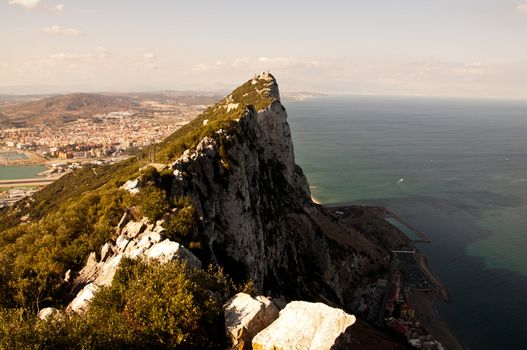 Steep rocky coastal lookout point ridge and cliffs overlooking ocean with a city in the distance.