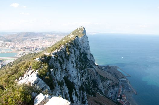 Steep rocky coastal lookout point ridge and cliffs overlooking ocean with a city in the distance.