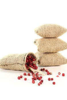 red peppercorns in a jute sack and bushels on white background