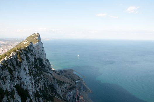 Steep rocky coastal lookout point ridge and cliffs overlooking ocean with a city in the distance.