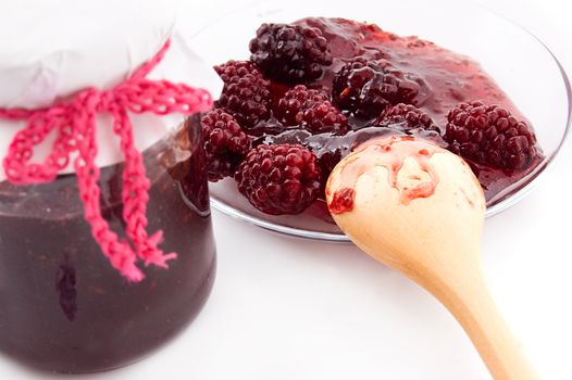 Blackberry jam in bottle and plate with wooden spoon, focus on spoon