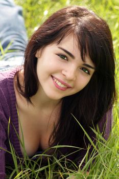 Close-up of a lovely young brunette with a bright, warm smile lying in a field of tall green grass.