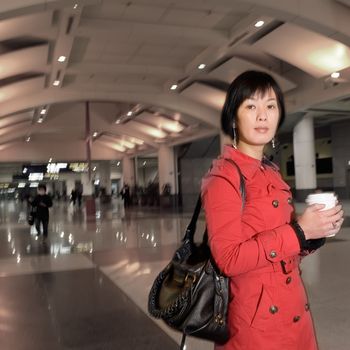 Asian woman holding cup of coffee, half length closeup portrait in modern public station.