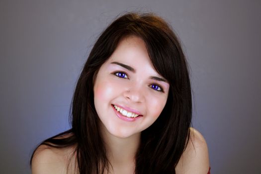 Studio close-up of a lovely young brunette with a bright, warm smile and electric-blue eyes.