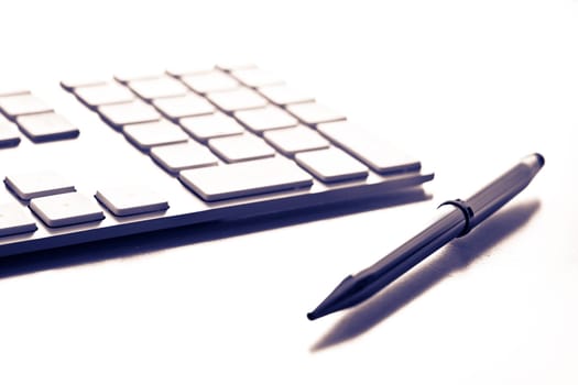 Shot of a white keyboard and a silver pen. Shallow depth of field. Great background for business designs.