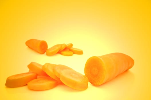 Close and low level capturing 2 partially sliced fresh organic carrot. Foreground carrot in focus. Yellow light effect background