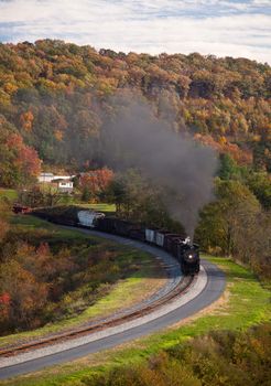 Old steam locomotive pulls freight through rural countryside in autumn