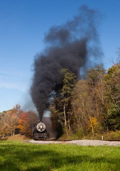 Old steam locomotive pulls freight through rural countryside in autumn