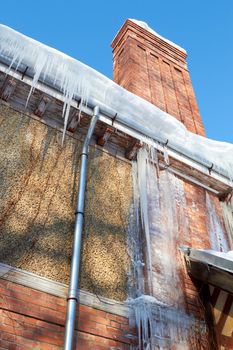 Icicles hanging from a dranpipe  of  house with chimney on a sky background