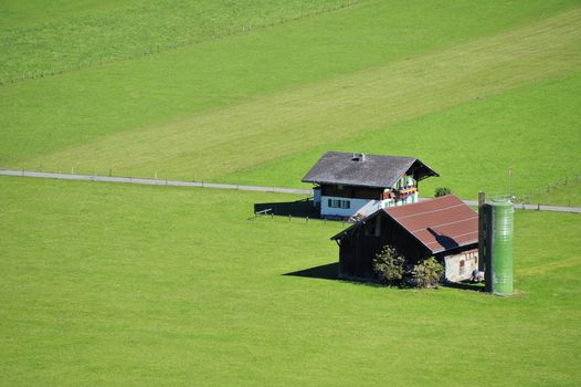 Aerial view of a small farm in Switzerland, set in green fields. Space for text on the green of the fields.
