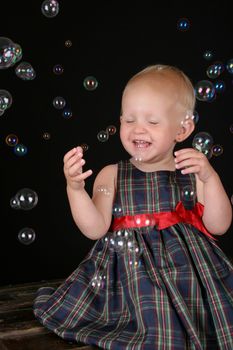 Cute blond toddler girl surrounded by bubbles sitting on a wooden trunk