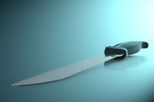 Close and low level angle capturing a stainless steel kitchen knife arranged over blue light effect filter