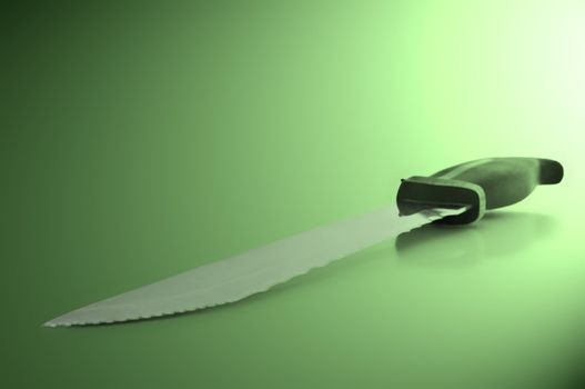 Close and low level angle capturing a stainless steel kitchen knife arranged over green light effect filter