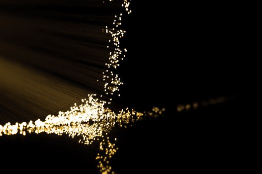 Close up on the ends of golden fibre optic light strands reflecting on black.