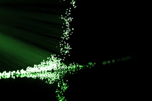 Close up on the ends of green fibre optic light strands reflecting on black.
